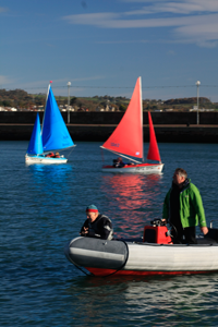 Red and Light Blue Access Dinghy Sailing in Carrickfergus Harbour with Fergus as Safety Boat